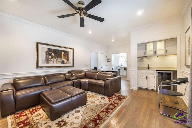 living room featuring ornamental molding, light wood-type flooring, ceiling fan, and indoor wet bar