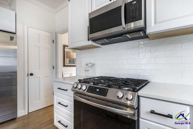 kitchen featuring dark wood-type flooring, ornamental molding, appliances with stainless steel finishes, tasteful backsplash, and white cabinetry