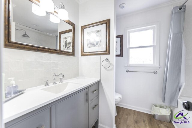 bathroom with vanity, backsplash, crown molding, hardwood / wood-style flooring, and toilet