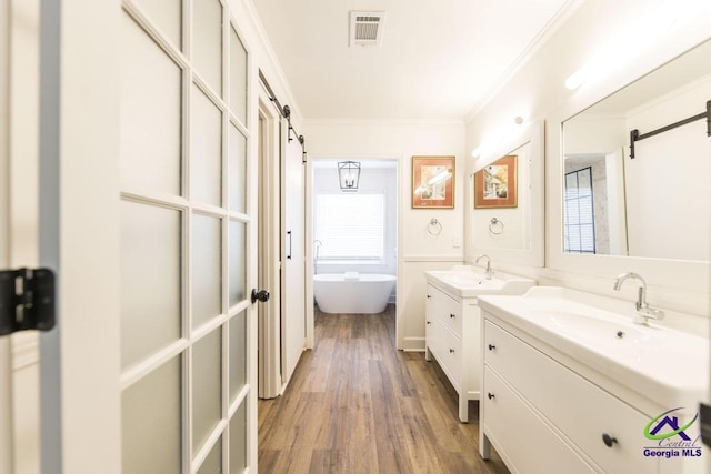 bathroom featuring hardwood / wood-style floors, vanity, ornamental molding, and a bathing tub