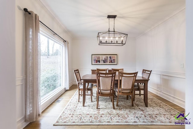 dining area with a notable chandelier, light wood-type flooring, and ornamental molding