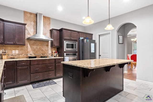 kitchen featuring a breakfast bar, wall chimney range hood, hanging light fixtures, light stone counters, and stainless steel appliances