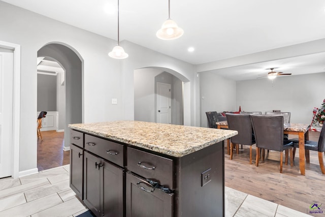 kitchen featuring light wood-type flooring, dark brown cabinets, ceiling fan, decorative light fixtures, and a kitchen island