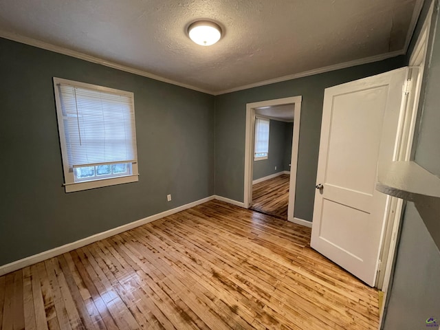 spare room featuring light wood-type flooring, a textured ceiling, and crown molding