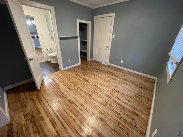 unfurnished bedroom featuring ensuite bathroom, a spacious closet, ornamental molding, and light hardwood / wood-style flooring