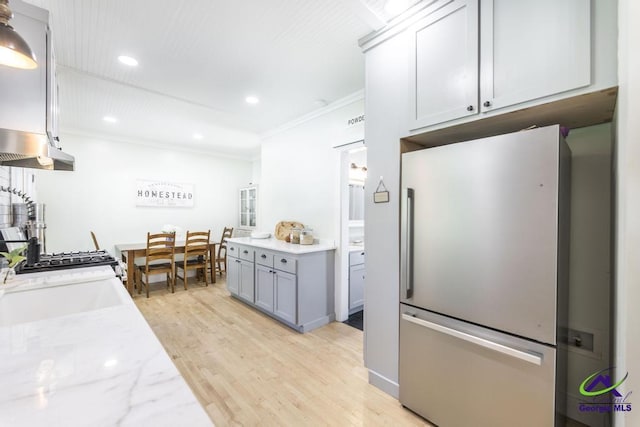 kitchen featuring sink, ornamental molding, light hardwood / wood-style floors, light stone counters, and stainless steel refrigerator