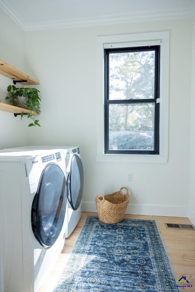 clothes washing area featuring washer and dryer, light wood-type flooring, and ornamental molding