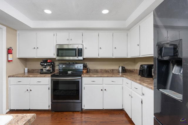 kitchen with appliances with stainless steel finishes, dark wood-type flooring, white cabinetry, and a textured ceiling