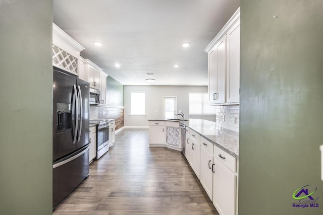 kitchen with stainless steel appliances, white cabinets, light stone counters, kitchen peninsula, and decorative backsplash