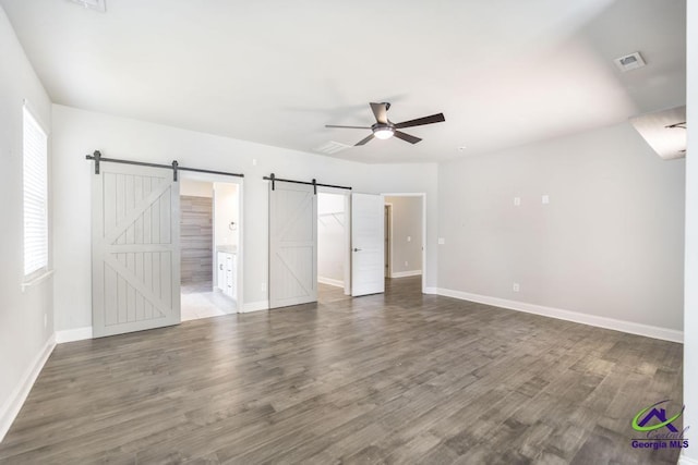 unfurnished bedroom with ensuite bathroom, ceiling fan, a barn door, and dark hardwood / wood-style floors