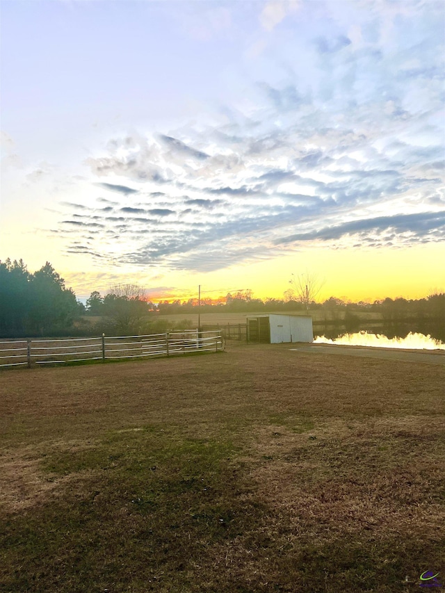 yard at dusk with an outbuilding, a rural view, and a water view