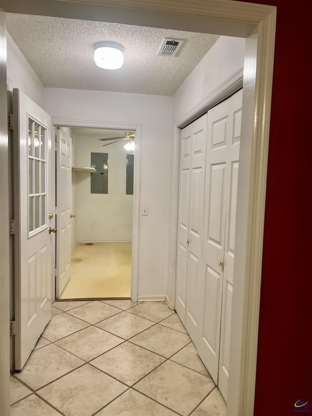 hall featuring a textured ceiling, electric panel, and light tile patterned floors