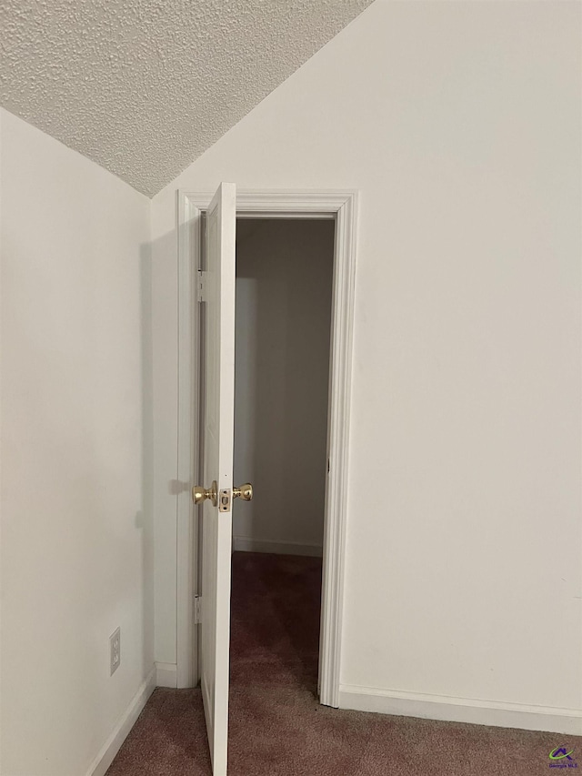 corridor with a textured ceiling, vaulted ceiling, and carpet floors