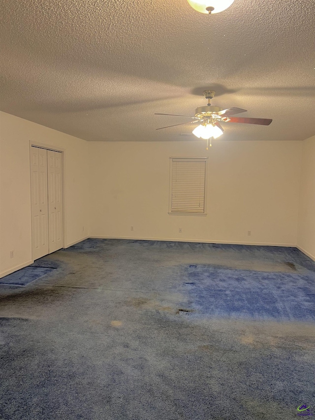 empty room with ceiling fan, a textured ceiling, and dark colored carpet