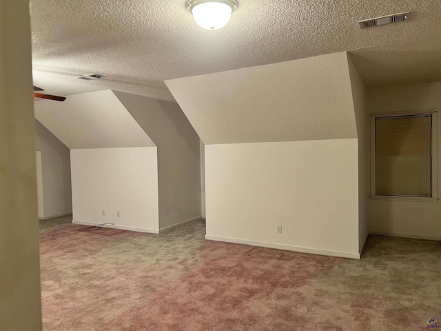 additional living space with light colored carpet, ceiling fan, vaulted ceiling, and a textured ceiling