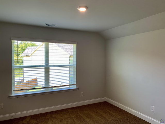 unfurnished room featuring dark colored carpet, vaulted ceiling, and a healthy amount of sunlight