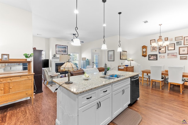 kitchen featuring pendant lighting, sink, white cabinetry, light stone countertops, and an island with sink