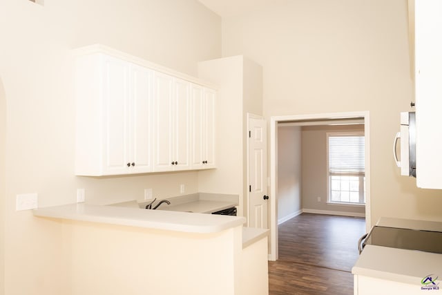 kitchen with kitchen peninsula, dark wood-type flooring, a high ceiling, and white cabinetry