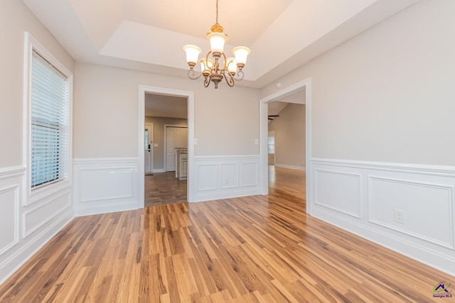 unfurnished room featuring an inviting chandelier, a raised ceiling, and wood-type flooring