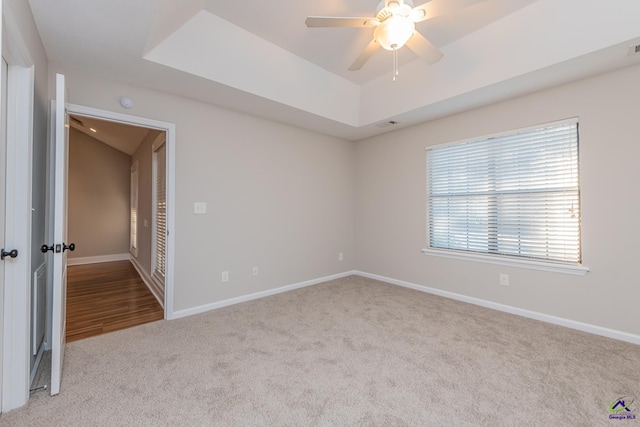 empty room featuring ceiling fan, light colored carpet, and a raised ceiling