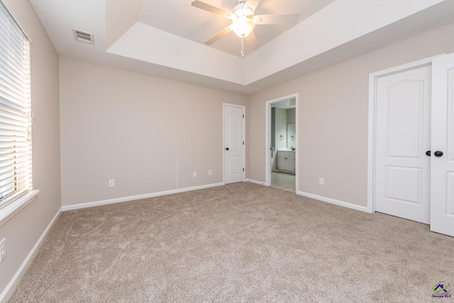 unfurnished bedroom with ceiling fan, ensuite bath, light carpet, and a raised ceiling