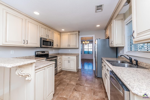 kitchen featuring appliances with stainless steel finishes, sink, cream cabinets, a notable chandelier, and light tile patterned floors