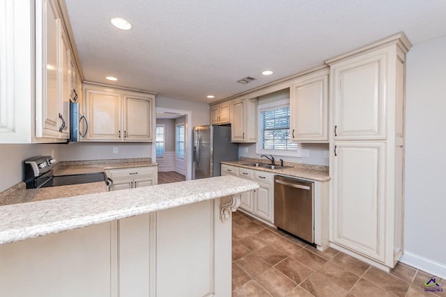 kitchen with kitchen peninsula, a kitchen bar, sink, appliances with stainless steel finishes, and cream cabinetry