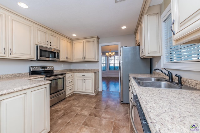 kitchen featuring appliances with stainless steel finishes, an inviting chandelier, sink, hanging light fixtures, and cream cabinets