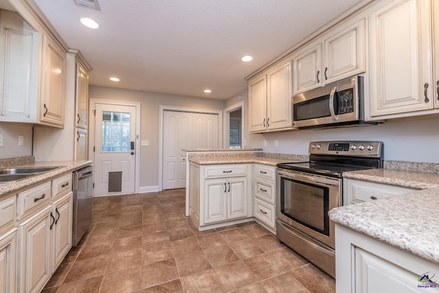 kitchen featuring stainless steel appliances, cream cabinetry, light stone counters, and sink