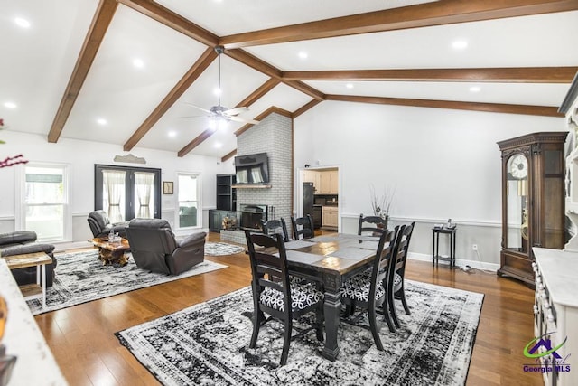 dining room featuring ceiling fan, dark hardwood / wood-style floors, a brick fireplace, beam ceiling, and french doors