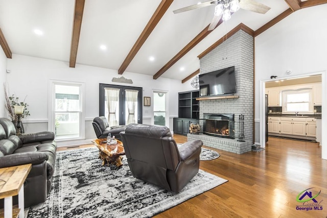 living room with wood-type flooring, vaulted ceiling with beams, a fireplace, sink, and ceiling fan