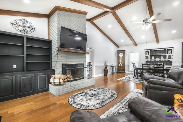 living room with a brick fireplace, wood-type flooring, vaulted ceiling with beams, and ceiling fan