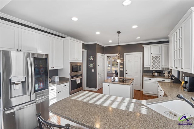 kitchen with appliances with stainless steel finishes, a kitchen island, decorative light fixtures, white cabinetry, and sink