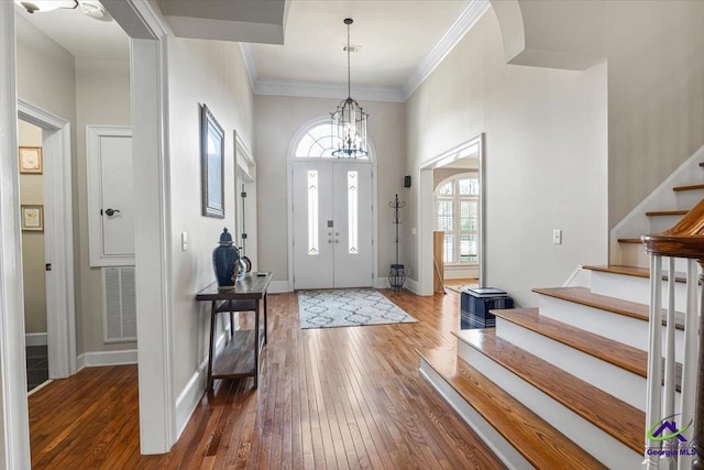 foyer entrance with dark wood-type flooring, ornamental molding, and a notable chandelier