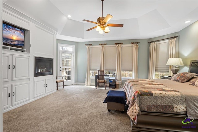 bedroom with light carpet, ceiling fan, and a tray ceiling