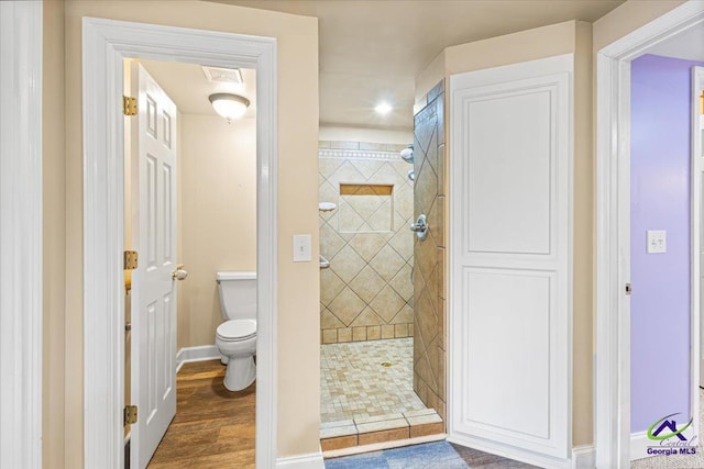 bathroom with hardwood / wood-style floors, toilet, and a tile shower