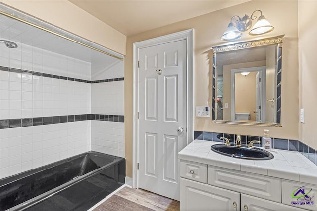 bathroom with tiled shower / bath combo, wood-type flooring, and vanity