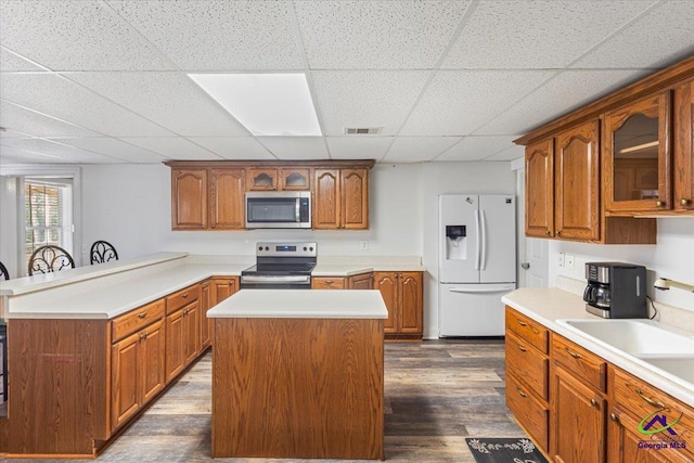 kitchen with a center island, a kitchen bar, a paneled ceiling, appliances with stainless steel finishes, and dark hardwood / wood-style flooring