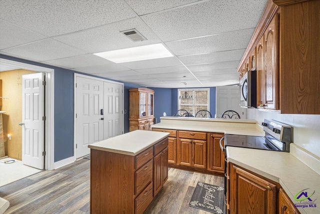 kitchen with a paneled ceiling, a kitchen island, dark wood-type flooring, stainless steel appliances, and a notable chandelier