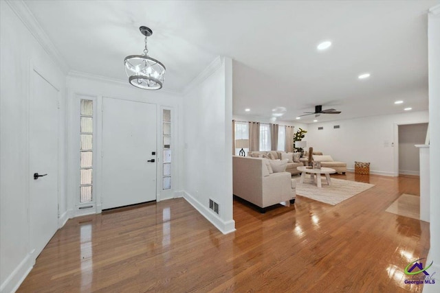 entrance foyer with crown molding, ceiling fan with notable chandelier, and wood-type flooring