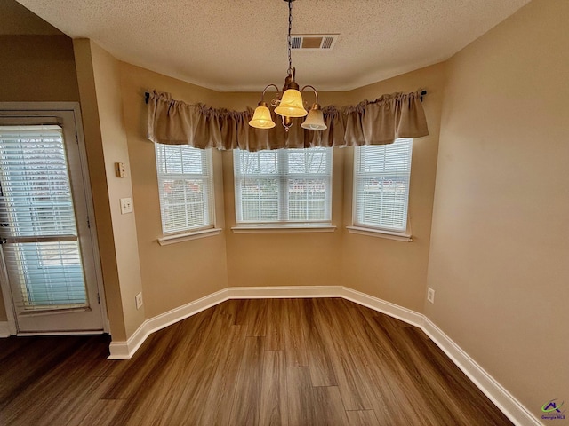 unfurnished dining area featuring a textured ceiling, an inviting chandelier, and wood-type flooring