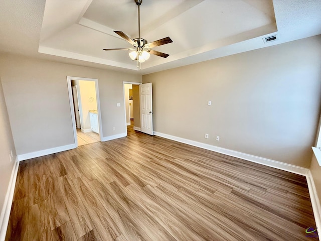 unfurnished bedroom featuring light wood-type flooring, ceiling fan, connected bathroom, and a raised ceiling