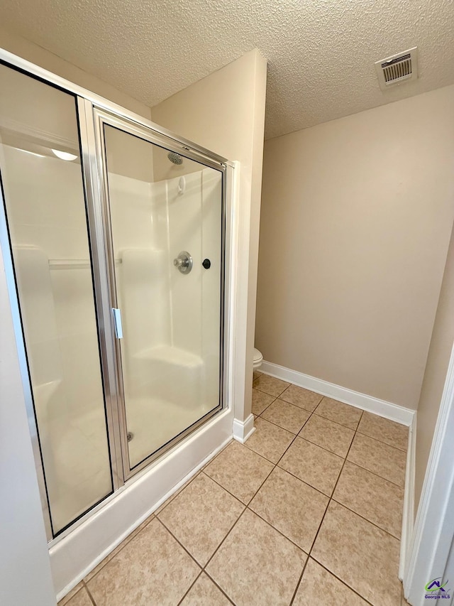 bathroom with a shower with shower door, tile patterned floors, toilet, and a textured ceiling