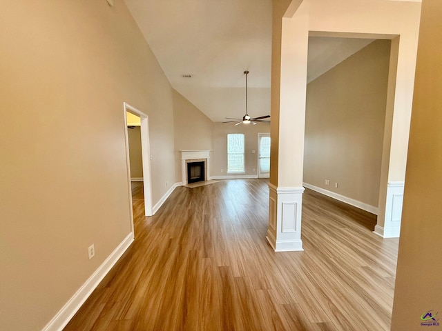 unfurnished living room featuring ceiling fan, light wood-type flooring, ornate columns, and high vaulted ceiling