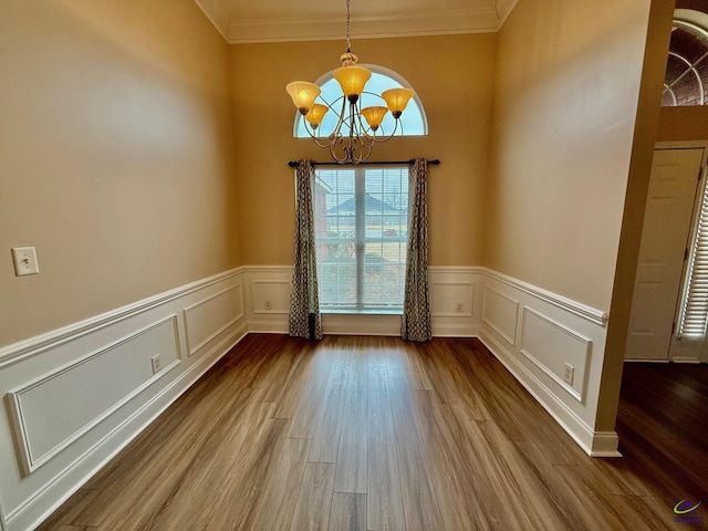 unfurnished dining area featuring an inviting chandelier, ornamental molding, and wood-type flooring