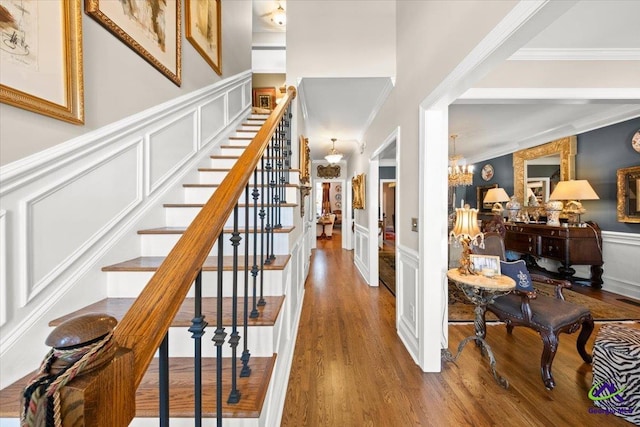 stairs featuring hardwood / wood-style flooring, crown molding, and a notable chandelier