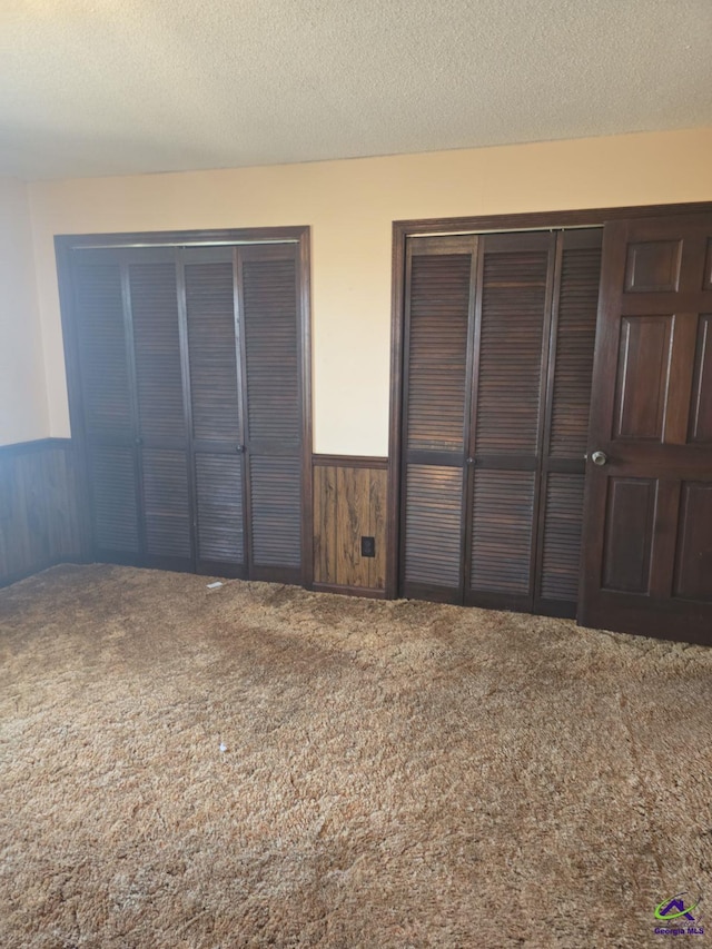 unfurnished bedroom featuring a closet, wood walls, a textured ceiling, and carpet flooring