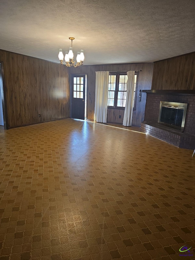 unfurnished living room with a brick fireplace, a textured ceiling, a notable chandelier, and wooden walls