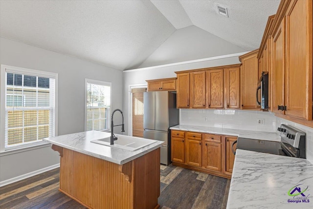 kitchen with a center island with sink, appliances with stainless steel finishes, backsplash, lofted ceiling, and sink