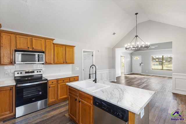 kitchen featuring an island with sink, stainless steel appliances, decorative backsplash, hanging light fixtures, and sink